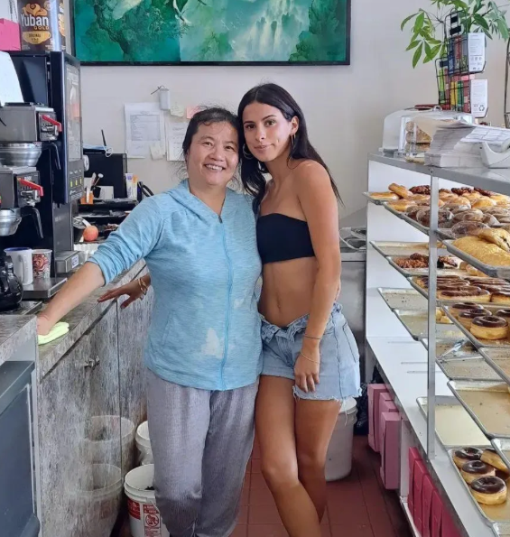 The owner of Donut House with a member of her team behind the counter, with the mountain mural and coffee station behind them